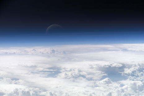 Durch die bläulich erscheinende Atmosphäre oberhalb eines Wolkenmeeres erkennt man die schwach schimmernde Mondsichel. (Quelle NASA Earth Oberservatory (https://eol.jsc.nasa.gov/SearchPhotos/photo.pl?mission=ISS013&roll=E&frame=54329))